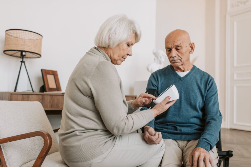 An elderly gentleman having his blood pressure checked by his wife.
